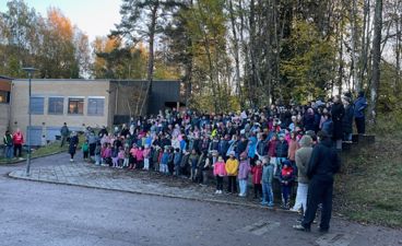 en gruppe mennesker som står på en vei med trær og en bygning