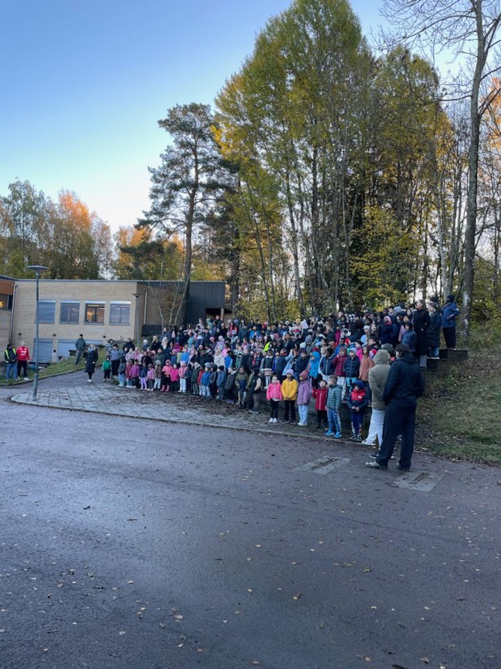 en gruppe mennesker som står på en vei med trær og en bygning